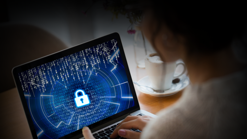 A business professional working at a desk with multiple monitors displaying cybersecurity data, including a lock icon and threat detection graphs. A digital shield and binary code overlay symbolize strong cybersecurity protection in a high-tech office environment.